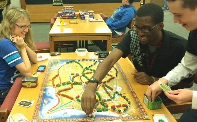 Meshach Adams makes a move playing Ticket to Ride as Kylie Gier and Nicholas Showalter look on.