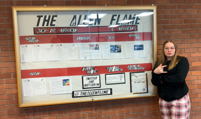 Alyssa+Winsler%2C+Student+Reporter+for+The+Allen+Flame%2C+poses+with+the+The+Allen+Flame+news+board+in+the+B+wing+of+Allens+main+building.+